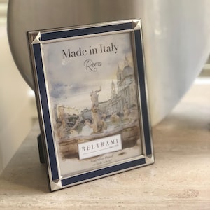 May include: A rectangular silver-plated picture frame with a dark blue border. The frame contains a print of a Roman fountain with the text Made in Italy, Roma, and BELTRAMI Since 1979, Real Silver Plated, cm 13x18 inch 5x7 printed on the paper.