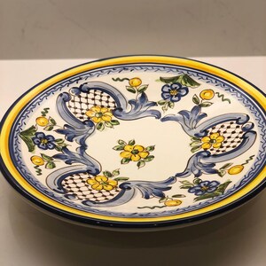 Puede incluir: Plato ovalado de cerámica con centro blanco y diseño floral azul, amarillo y negro. El plato tiene un borde amarillo y azul. El diseño incluye flores amarillas, hojas azules y un patrón de enrejado.