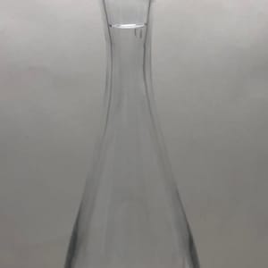 Puede incluir: Una decantador de vidrio transparente con un tapón de vidrio texturizado. La decantador tiene un cuerpo redondo y un cuello largo y delgado.