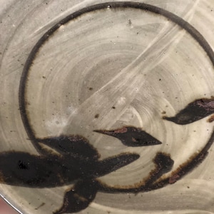 May include: A ceramic plate with a light grey glaze and a black design of stylised leaves. The plate is circular and has a slightly raised rim.