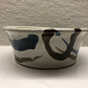 May include: A white ceramic bowl with brown and blue abstract designs. The bowl has a rounded shape and a slightly flared rim.