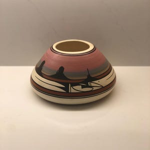 Peut inclure: Un vase en céramique fait à la main, avec une base large et une ouverture étroite. Le vase présente un motif avec des bandes horizontales de couleurs, dont le rouge, le rose et le noir, avec une base crème. Le vase a une forme arrondie unique.