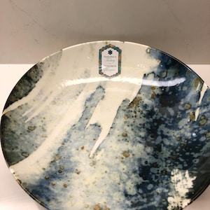 May include: A shallow round bowl featuring a marbled pattern in shades of deep blue, white, and metallic gold. A rectangular label is affixed to the inner rim, displaying the text Handcrafted in Turkey and Fait à la main en Turquie.