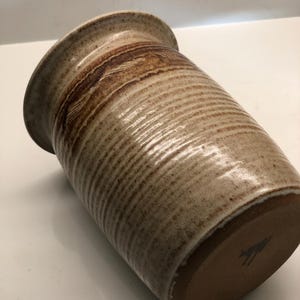 May include: A brown and white ceramic utensil holder with a textured, striped design.