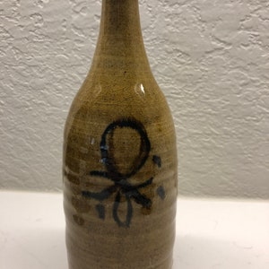 Può includere: Una bottiglia di ceramica marrone con un disegno nero di un polpo stilizzato sul davanti.