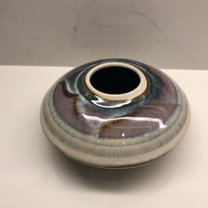 Puede incluir: Un pequeño jarrón redondo de cerámica con un esmalte multi-color en espiral. El esmalte presenta tonos de azul, verde, marrón y morado.