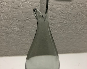May include: A gray glass vase with a unique, abstract design. The vase has a narrow neck and a wide, rounded base.