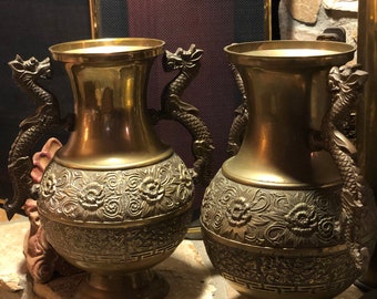 May include: Two ornate gold vases with dragon handles and intricate floral designs. The vases are sitting on a stone surface.