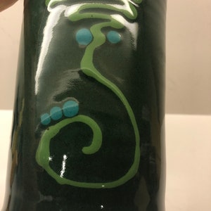May include: A dark green ceramic vase with a white and green abstract design. The vase has a glossy finish and is decorated with blue dots.