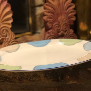 Può includere: Un vassoio ovale con superficie bianca e bordo blu. Il vassoio è decorato con forme astratte blu, verdi e grigie. Il vassoio è posto su una superficie di pietra.