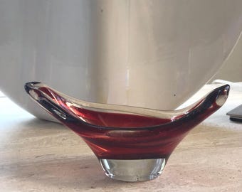 Könnte beinhalten: Eine kleine, klare Glasschale mit tiefrotem Innenraum und klarem Boden. Die Schale hat eine einzigartige, geschwungene Form mit spitzen Kanten. Die Schale steht auf einer hellen, strukturierten Oberfläche.