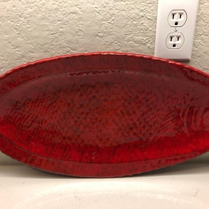 Puede incluir: Una fuente de servir de cerámica roja con forma de pez. La fuente tiene una superficie texturizada y un acabado brillante.