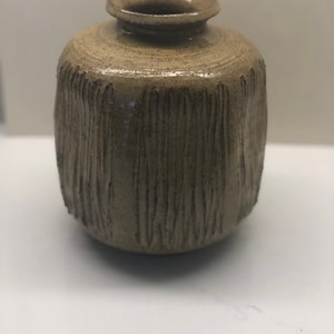 May include: A small, brown ceramic vase with a textured, vertical pattern. The vase has a rounded body and a slightly flared opening.
