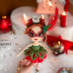 May include: A handcrafted crochet doll with a festive design. The doll has a red and green dress, a decorative headpiece, and a mask. The text "PATTERN CROCHET PDF" is visible. The doll is held in front of a blurred background with candles and ornaments.
