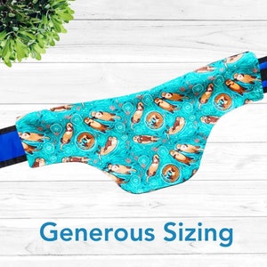 May include: A turquoise blue fabric dog collar with a pattern of brown otters holding hands. The collar has black trim and blue webbing. The text "Generous Sizing" is printed below the collar.