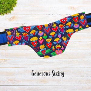 May include: A black fabric neck gaiter with a colorful pattern of hearts, flames, and eyes. The pattern is on a dark blue background. The gaiter has a blue elastic band.