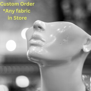 May include: A white mannequin head with a smooth, shiny surface. The head is tilted upwards, and the mouth is slightly open. The text "Custom Order *Any fabric in Store" is visible in the background.