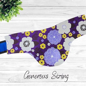 May include: Purple fabric dog bandana with a floral pattern in shades of white, yellow, and purple. The bandana has a blue trim and the text "Generous Sizing" is printed below the bandana.