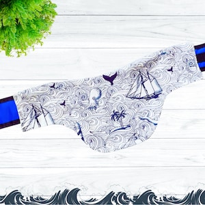 May include: A white fabric neck gaiter with a blue and white nautical pattern featuring an octopus, a sailboat, and waves. The gaiter has blue trim on the edges.