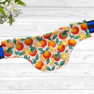 May include: A patterned fabric with a repeating design of oranges and green leaves. The oranges are a vibrant orange color, with some sliced to reveal the juicy interior. The fabric has a cream-colored background and is trimmed with blue and black fabric.