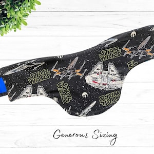 May include: Black fabric neck warmer with a Star Wars print featuring X-wing fighters and the Millennium Falcon. The fabric has a black background with white stars and yellow text that reads "Star Wars".