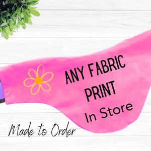 May include: Pink fabric dog bandana with a yellow daisy and the text "ANY FABRIC PRINT In Store Made to Order".