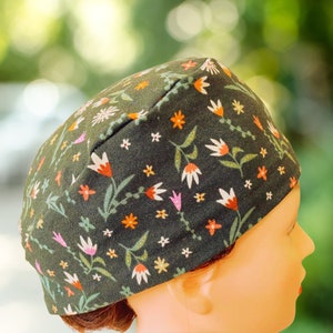 May include: A dark green scrub hat with a floral print featuring small white, orange, and pink flowers. The hat is made of a soft, comfortable fabric and is perfect for healthcare professionals.