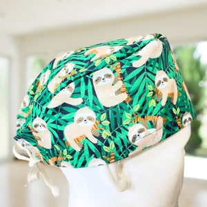 May include: A green, black, and brown scrub hat with a pattern of sloths hanging from trees. The hat has a drawstring tie.