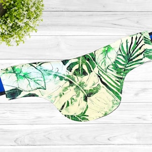 May include: A green and white bandana with a tropical leaf pattern. The bandana has a blue trim around the edges.