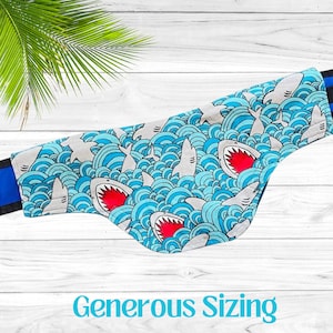 May include: A blue and white dog bandana with a shark and wave pattern. The bandana has a blue trim and the text "Generous Sizing" is printed below the bandana.