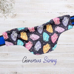 May include: A black fabric item with a colorful heart pattern, including pink, yellow, blue, and purple hearts. The item has a blue strap and the words "Generous Sizing" in cursive.