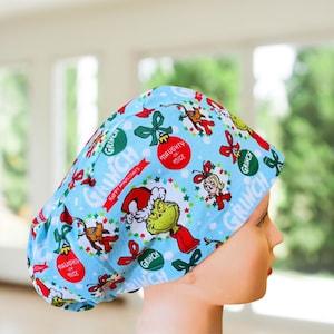 May include: A blue scrub hat with a festive Grinch print. The hat features the Grinch, Cindy Lou Who, and other characters from the classic Christmas story. The hat also includes the text "Grinch" and "Naughty or Nice".