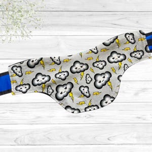 May include: A gray pet bandana with a repeating pattern of cartoon clouds and yellow lightning bolts. The bandana has a blue and black strap. The background is a white wooden surface.