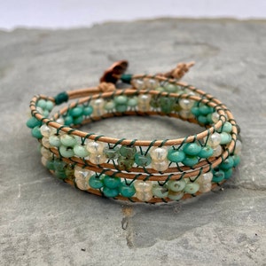 May include: A triple-wrap bracelet with green and white beads, woven with brown leather cord.