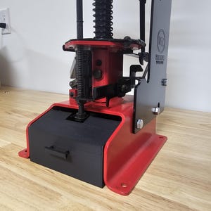 May include: A red and black MEC 9000 Series reloading press. The press has a black base with a drawer, a red frame, and various black components. The MEC logo is visible on the side. The press is designed for reloading ammunition.