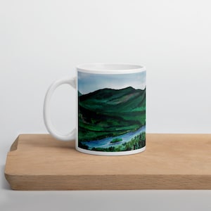 May include: White ceramic mug with a scenic image of a river winding through a lush green valley with mountains in the background.