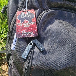 May include: Black backpack with a sparkly finish, featuring a tag that reads "D2 Summit 2020" and the name "Emma." The backpack also has two small silver tags that say "chasse."