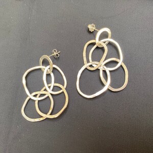 Puede incluir: Un par de pendientes de plata con un grupo de círculos interconectados. Los pendientes están hechos de metal texturizado y tienen un diseño moderno y minimalista.