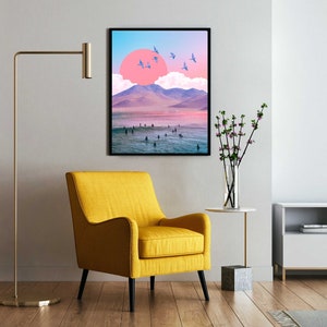 May include: A framed print of a surreal landscape with a pink sun, mountains, and a beach with people in the water. The print is in a black frame and is hanging on a white wall.