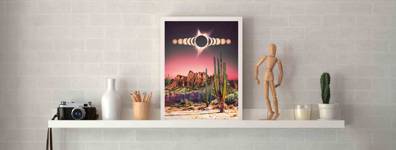 May include: A framed print of a desert landscape with a sunset sky and a solar eclipse. The eclipse is shown in stages, with the moon passing in front of the sun. The desert scene features tall cacti and rocky mountains.