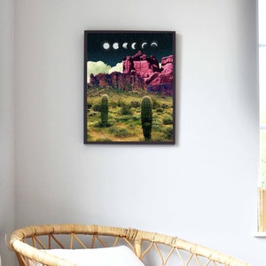 May include: A framed print of a desert landscape with a pink mountain range and two cacti in the foreground. The sky is dark blue with white clouds and a series of white crescent moons.