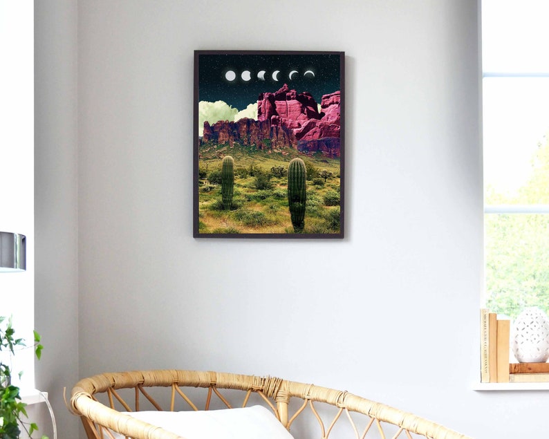 May include: A framed print of a desert landscape with a pink mountain range and two cacti in the foreground. The sky is dark blue with white clouds and a series of white crescent moons.