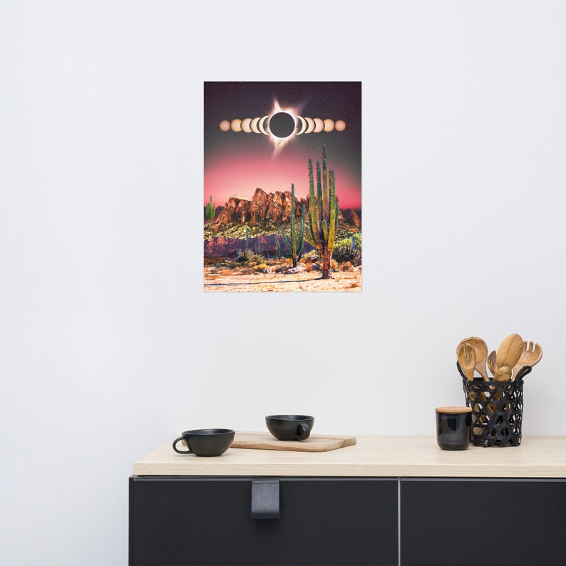 May include: A digital art print featuring a desert landscape with tall cacti and a pink sky. The sun is partially eclipsed by the moon, creating a ring of light in the sky.