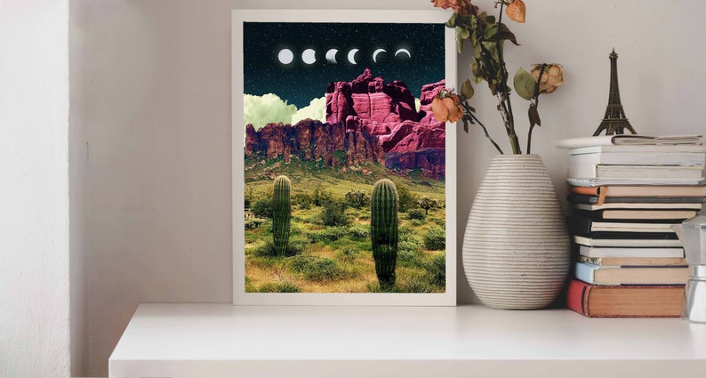 May include: A framed print of a desert landscape with two tall cacti in the foreground. The background features a mountain range with a pink hue and a night sky with a crescent moon and stars.