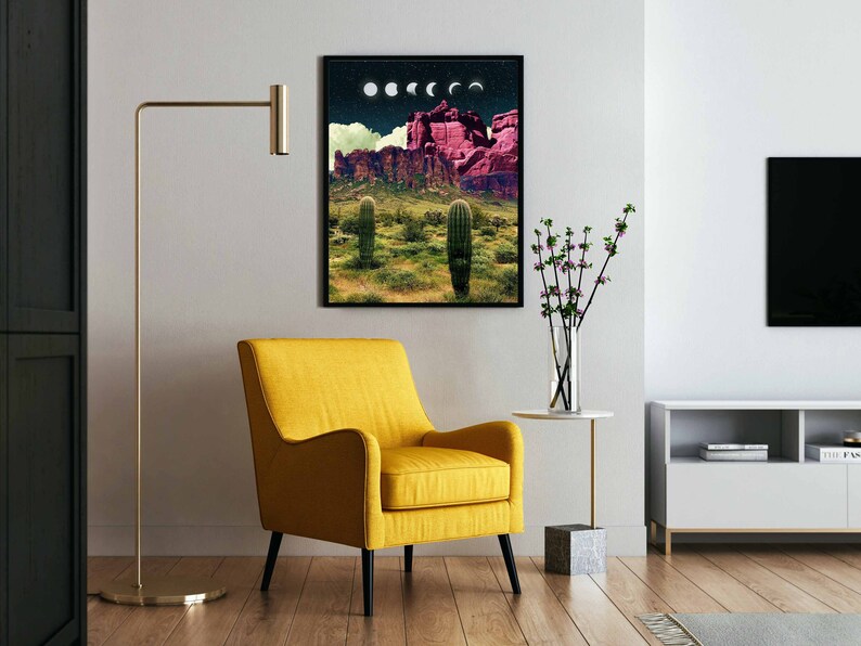 May include: A framed print of a desert landscape with a pink mountain range, cacti, and a crescent moon in the sky. The print is hanging on a white wall in a living room setting.