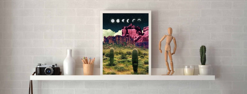 May include: A framed print of a desert landscape with a pink mountain range and cacti in the foreground. The sky is dark blue with white and gray moons in various phases.