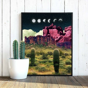 May include: A framed print of a desert landscape with a pink mountain range in the background. The sky is dark blue with white clouds and a series of white crescent moons.