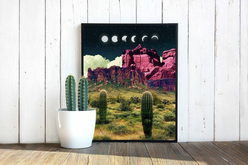 May include: A framed print of a desert landscape with a pink mountain range in the background. The sky is dark blue with white clouds and a series of white crescent moons.