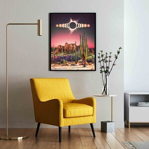 May include: A framed print of a desert landscape with a large black circle in the sky, surrounded by smaller circles. The landscape is a mix of red, brown, and green colors. The print is hanging on a white wall in a living room setting.