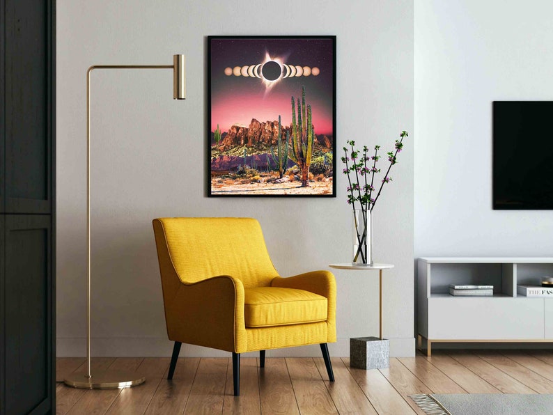 May include: A framed print of a desert landscape with a large black circle in the sky, surrounded by smaller circles. The landscape is a mix of red, brown, and green colors. The print is hanging on a white wall in a living room setting.